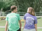 Two people sit on a park bench facing away from the viewer. A stylized map of Brantford appears on the backs of their t-shirts